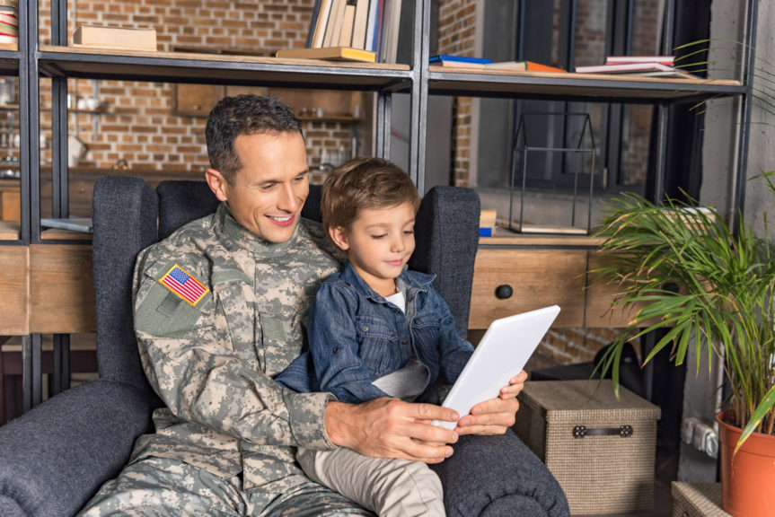 Father in military uniform reading to his son on a mobile device