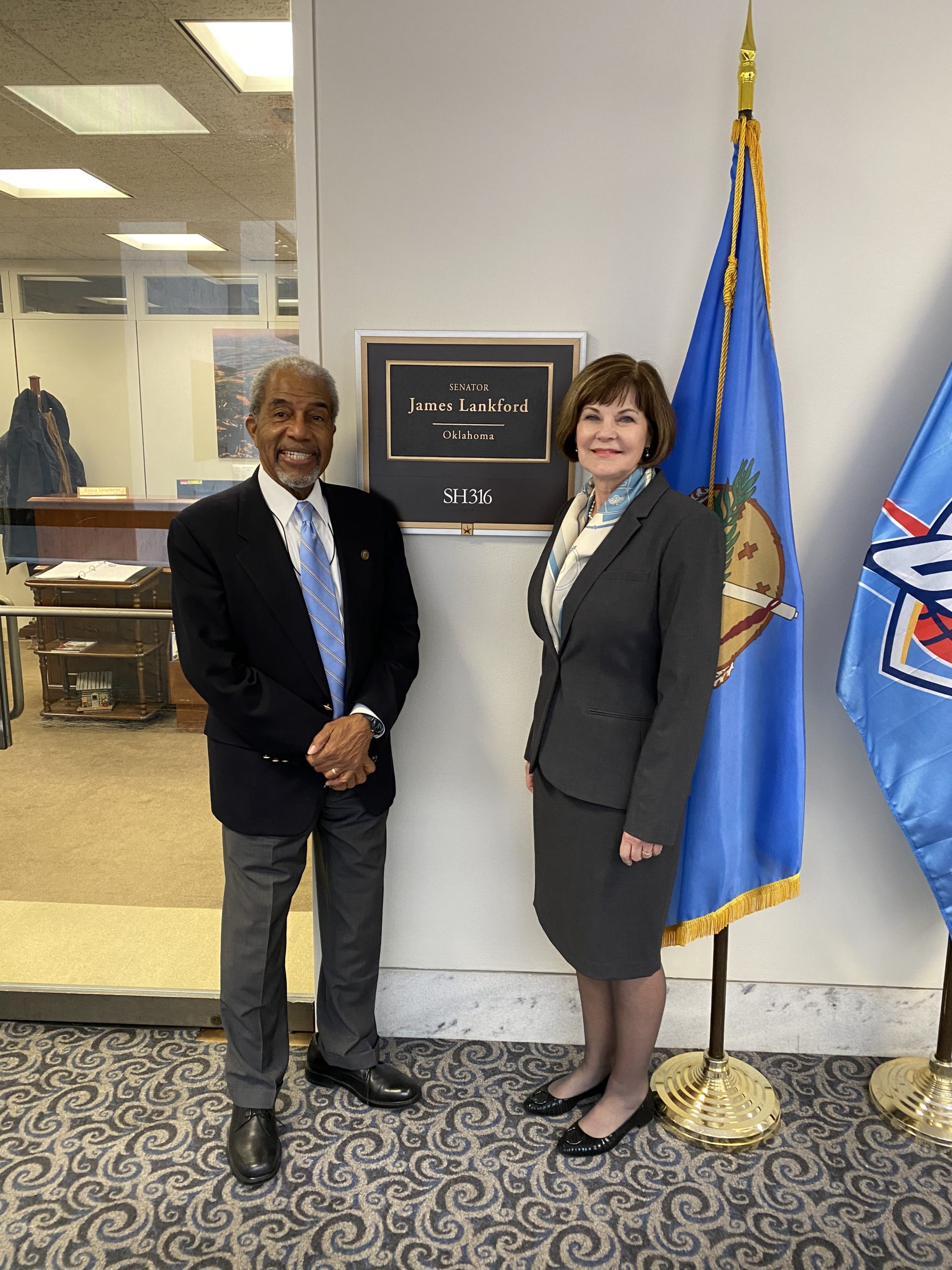 Captioned telephone and vietnam veteran Robert Richardson and Loretta Herrington from WID stand on either side of plaque outsdie Senator Lankford's office